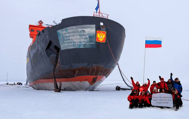 Люди с флагом стоящие на льду перед ледоколом